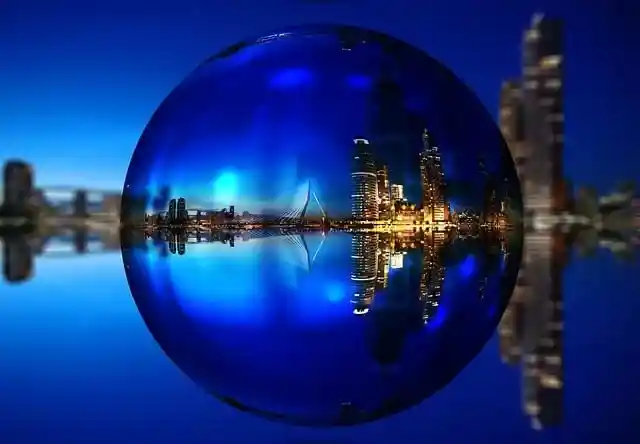 Nachtfoto van de Erasmusbrug en de Wilhelminapier in Rotterdam, gezien door een glazen bol, met de stad prachtig weerspiegeld.